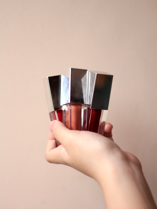 三本のリップグロスを持っている人の手の写真